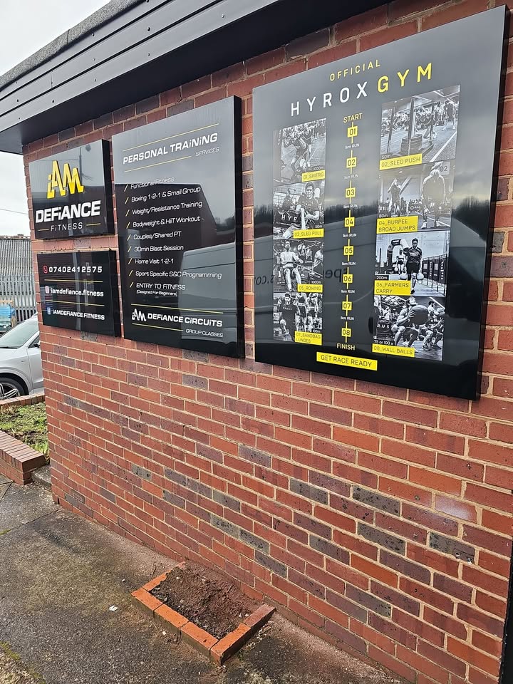 Signage boards on the exterior brick wall of the gym unit, including an Official HYROX Gym board